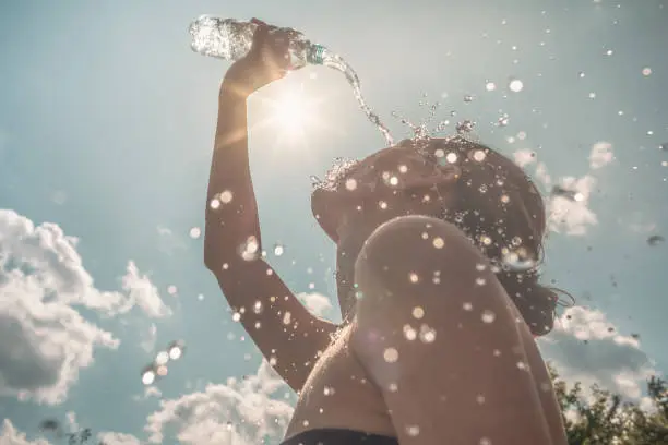 Woman cooling down splashing herself with bottle of water on a hot sunny day.