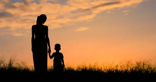 Photo of Mother and son walking in the field at sunset.