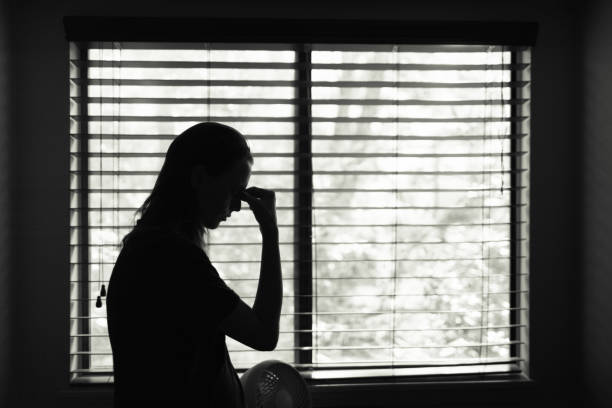 寝室の窓の隣に立っている疲れた女性。 - 喪失 写真 ストックフォトと画像