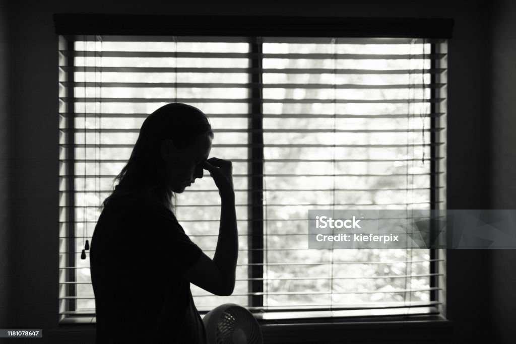 Tired woman standing next to bedroom window. Stressed young woman in the bedroom. Domestic Violence Stock Photo