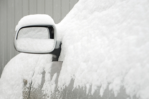 Car covered with snow. Car mirror in the snow. Abnormal weather. Winter in October. Early winter. Meteorology background. Forecast for cold season. Car service in cold weather. Temperature below zero.