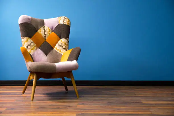 Photo of Empty modern chair on wooden floor. Solid wall with contrast baseboard background. One object of interior. Vintage chair on wooden legs. Scandinavian interior with multi-colored chair