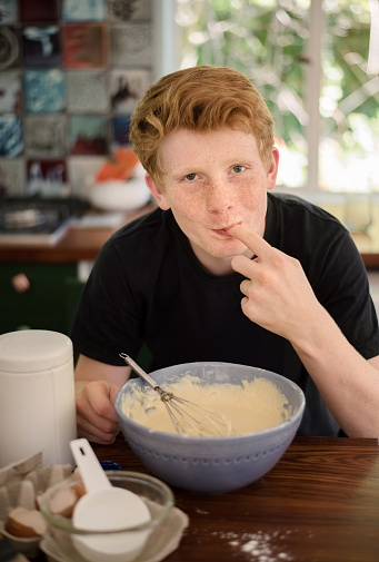 Shot of a young boy licking batter while preparing breakfast
