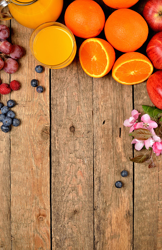 Orange juice, fresh oranges, apples, grapes, raspberries, blueberries and spring flowers on a wooden table - view from above - vertical photo