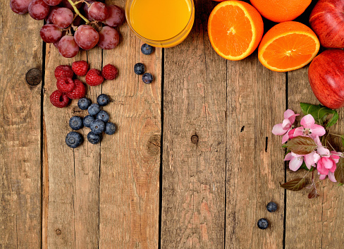 Orange juice, fresh oranges, apples, grapes, raspberries, blueberries and spring flowers on a wooden table - view from above