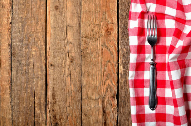 istock Fork on red checkered tablecloth right frame on vintage wooden table background - view from above 1181101891