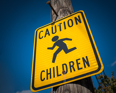 A warning street sign reads Caution Children against a blue sky