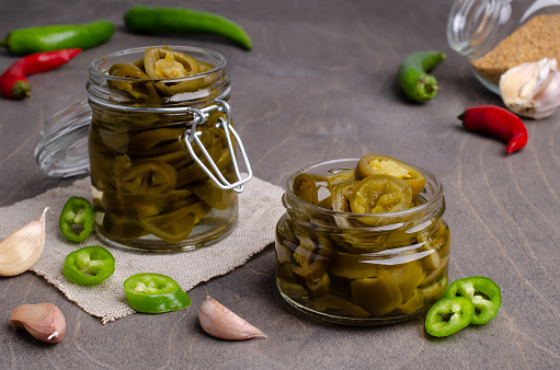 Pickled jalapeno slices in a glass jar on a wooden background. Selective focus.