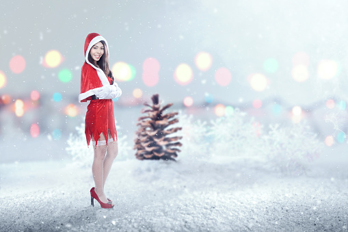 Asian woman in Santa costume standing when snowfall with blurred lights background