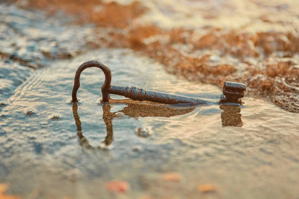 uma chave perdida oxidada velha do tesouro, encontrando-se na areia na ressaca na praia. o conceito de sorte e riqueza inesperada. - treasure luck treasure chest wealth - fotografias e filmes do acervo