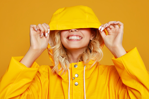 joven chica emocional feliz riendo con impermeable con capucha sobre fondo amarillo de color photo