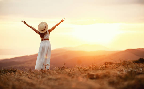 szczęśliwa kobieta stojąca z powrotem na zachodzie słońca w przyrodzie - liberation zdjęcia i obrazy z banku zdjęć