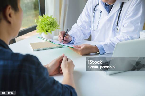 Doctor Using A Clipboard To Fill Out A Medical History Of A Young Mans Medication And Patient Discussing The Results Of A Physical Examination In A Clinic Stock Photo - Download Image Now