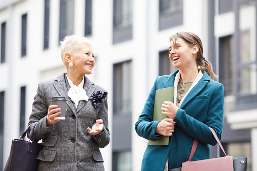 Two successful businesswomen talking to each other while walking along the street in the city