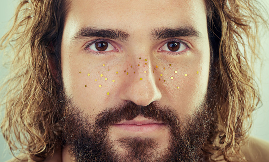 Studio shot of a handsome young man with glittery sequins on his face