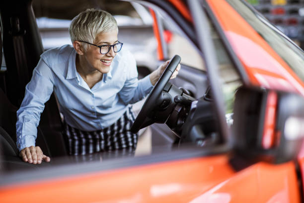 Happy mature woman buying a car in a showroom. Happy senior woman looking at car interior while shopping in a showroom. car ownership photos stock pictures, royalty-free photos & images