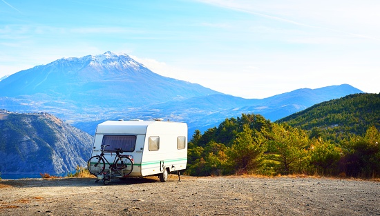 Caravan with a bike parked on a mountaintop with a view on the french Alps near lake Lac de Serre-Poncon on a bright sunny day