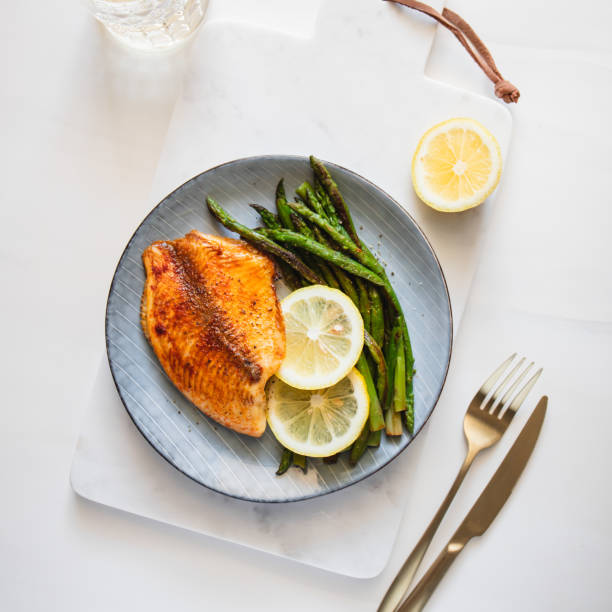 gebratener tilapiafisch mit spargel auf einem weißen marmortablett. gesunde mediterrane ernährung mittag- oder abendessen. ansicht von oben, flach liegend. - tilapia stock-fotos und bilder