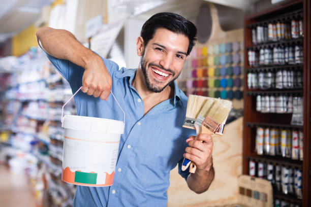 istock Man standing amongst racks in paint store with brushes and paint 1181152513