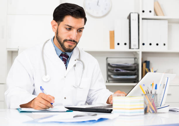 istock Spanish man doctor is working with documents behind laptop 1181152773