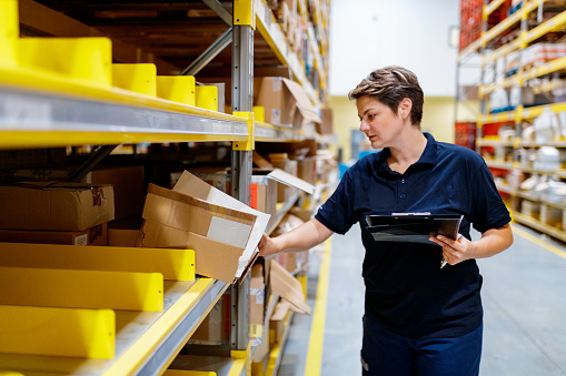 Female warehouse worker holding checklist and checking content of box in warehouse