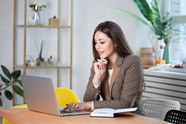 istock Young brunette woman working on a laptop in a bright comfortable office. 1181161858