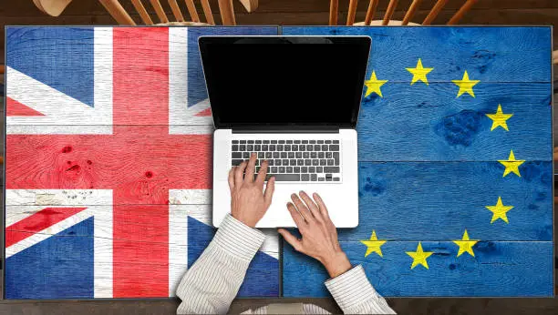 Photo of European and UK flagged wooden Table with laptop