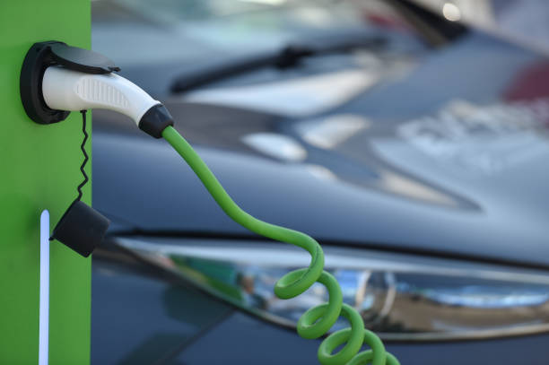 istock Electrical car plugged through a charging cable to a charging station. 1181163251