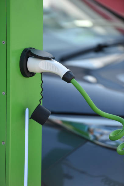 istock Electrical car plugged through a charging cable to a charging station. 1181163410