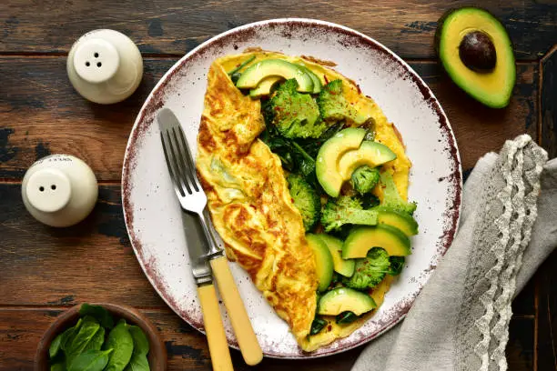 Omelette stuffed with green vegetables : broccoli, avocado and baby spinach on a plate on a dark wooden background.Top view with copy space.