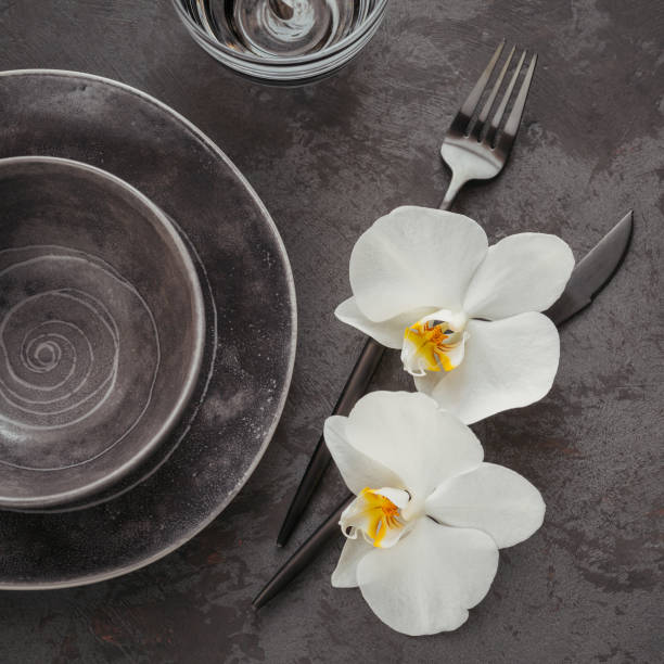 istock Elegance table setting with knitted grey napkin, cutlery, ceramic plates, glasses and white orchid flowers 1181169815