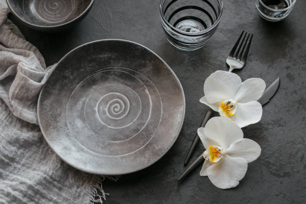 istock Elegance table setting with knitted grey napkin, cutlery, ceramic plates, glasses and white orchid flowers 1181169819