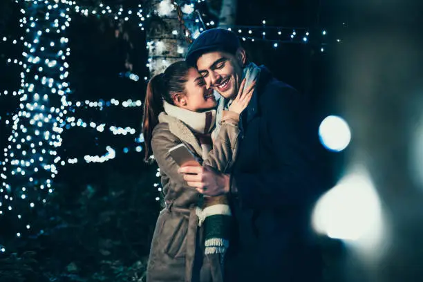 Couple using phone and enjoying Christmas spirit outdoors