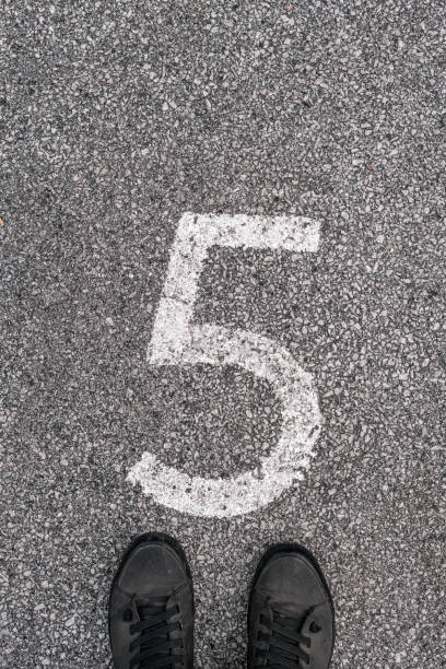 istock Man standing above number five imprint on asphalt road 1181171975