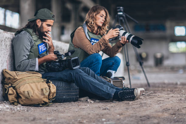 War journalists sitting in war zone Man and woman, war journalist with cameras at the place of action in war zone, taking a break. tv reporter photos stock pictures, royalty-free photos & images
