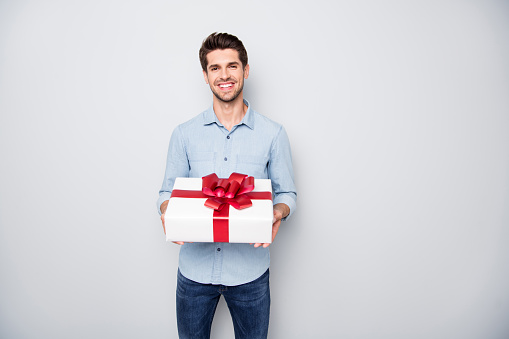 Portrait of positive charming lover man hold gift box present for 14-february, 8-march feel content enjoy holiday wear style denim jeans clothing isolated over grey color background