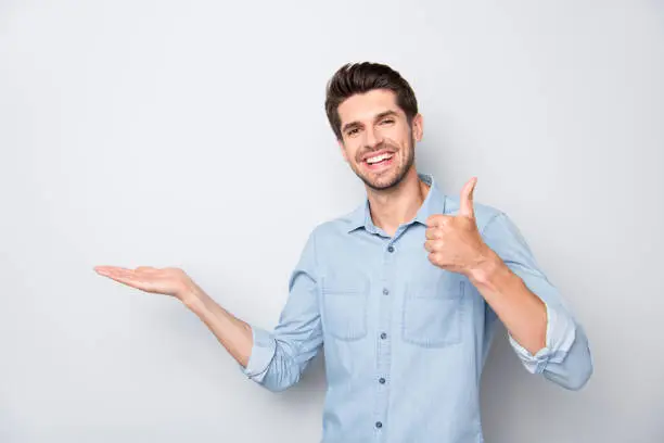 Portrait of positive cheerful man hold hand show thumb-up sign recommend, ads display promo wear casual style outfit isolated over grey color background