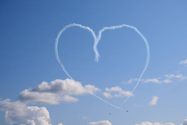 istock Two white and red passenger planes flying towards one another after making a loop in the sky and emiting some smoke or fumes making the shape look like a human heart seen on a cloudy summer day 1181176795