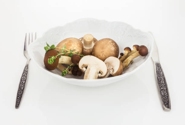 Button mushrooms and brown beech mushroom in bowl with fork and knife, on white background.