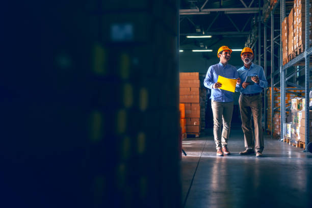 istock CEO going around warehouse with supervisor and talking analyzing sale statistics. Younger man holding folder with data while older one holding tablet. Both having yellow helmets. 1181190978