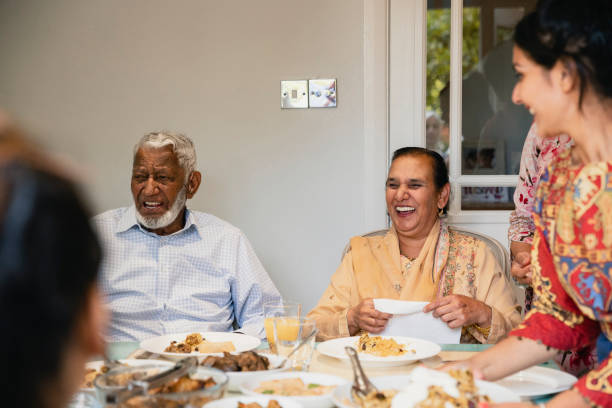 Dinner And Laughing A front-view shot of an Indian family sitting around the dining table enjoying their food, they are laughing and smiling. indian dinner stock pictures, royalty-free photos & images