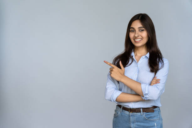 confident smiling indian young woman professional student customer saleswoman looking at camera pointing at sales copy space isolated on grey studio background, happy lady showing aside portrait - povo indiano imagens e fotografias de stock