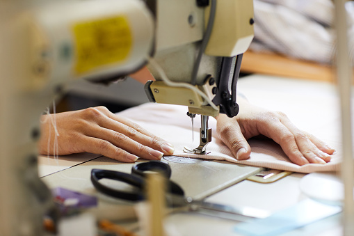 Close-up of woman working with fabric and she sewing with the help of sewing machine at her workplace