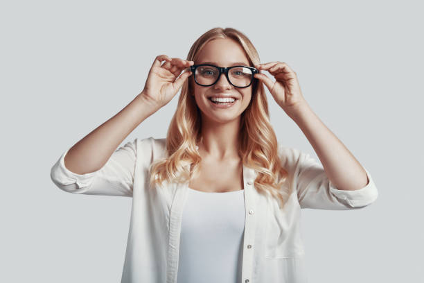 istock Attractive young woman adjusting eyewear and smiling while standing against grey background 1181202519