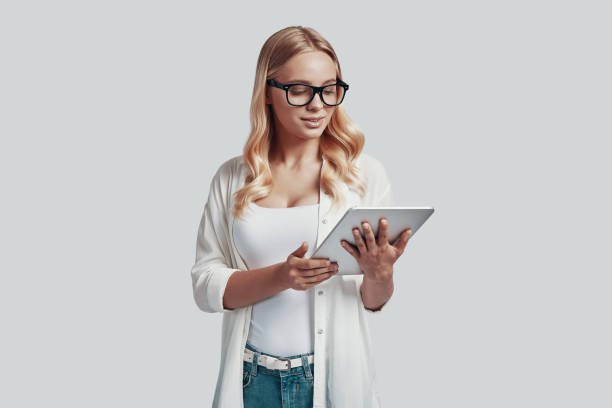 istock Attractive young woman in eyewear using digital tablet while standing against grey background 1181203033