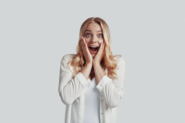 istock Shocked young woman looking at camera and making a face while standing against grey background 1181206784