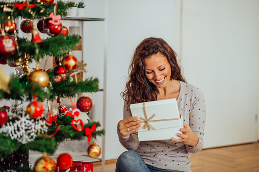 Portrait of attractive smiling woman opening her present for Christmas or New year.