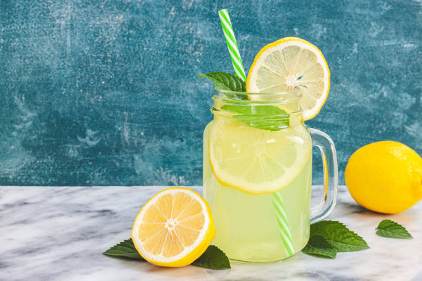 limonata al limone in barattolo di muratore con limoni e paglia sullo sfondo del tavolo - hot drink alcohol green glass foto e immagini stock