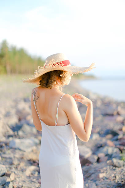 istock Back view of girl in hat walking on shingle beach 1181209021