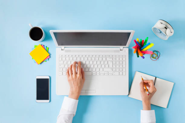 Overhead shot of woman working on laptop Woman hand taking notes to notebook while working on laptop computer. Blue table, top view. Flat-lay design. knolling concept stock pictures, royalty-free photos & images